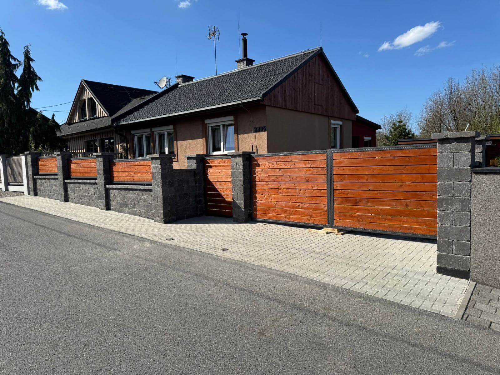 Nový plot z tmavých betonových tvárnic s dřevěnou výplní a posuvnou bránou před rodinným domem