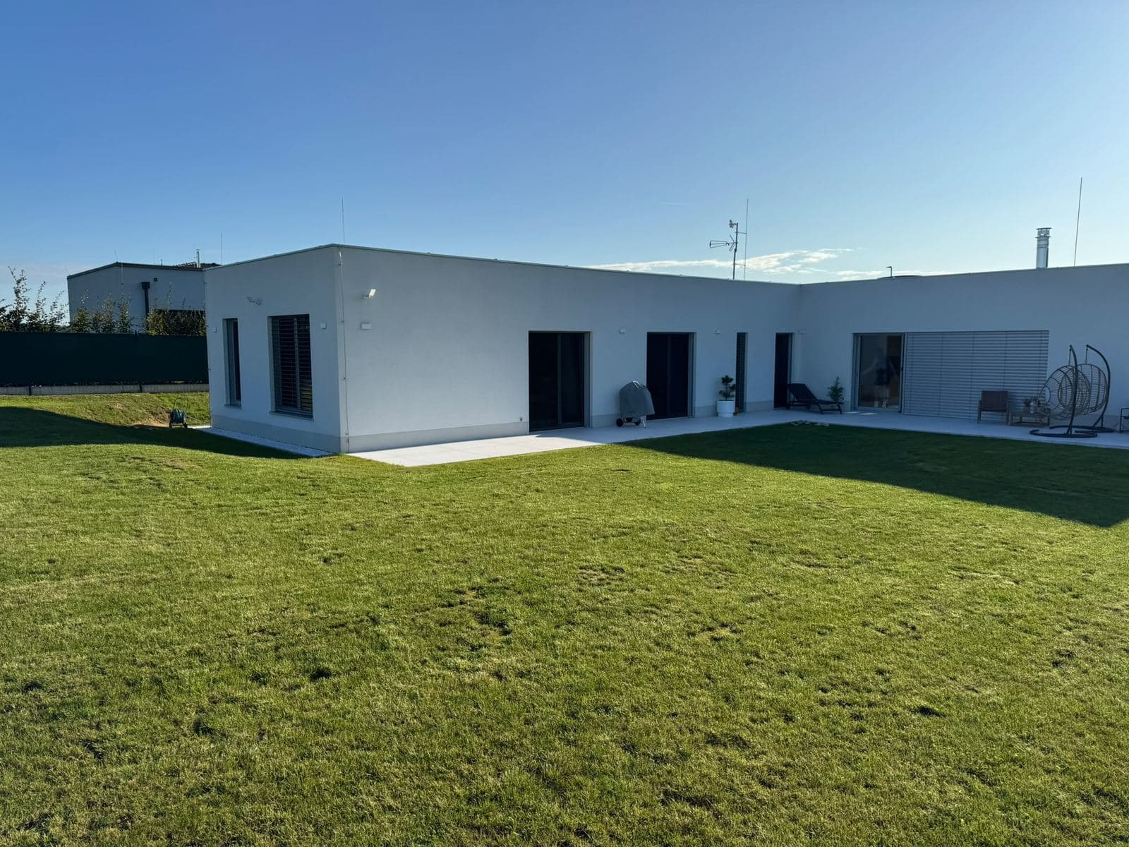 Moderní bungalov do tvaru L s plochou střechou, bílou fasádou a terasou
