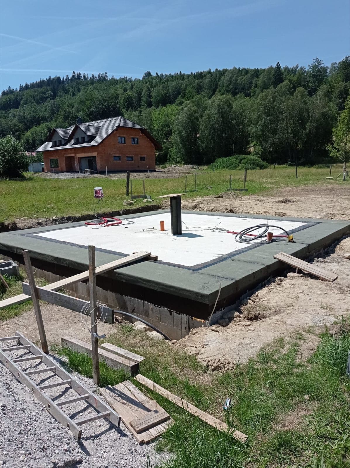 Hotová základová deska s hydroizolací a vyvedenými instalacemi na zelené louce